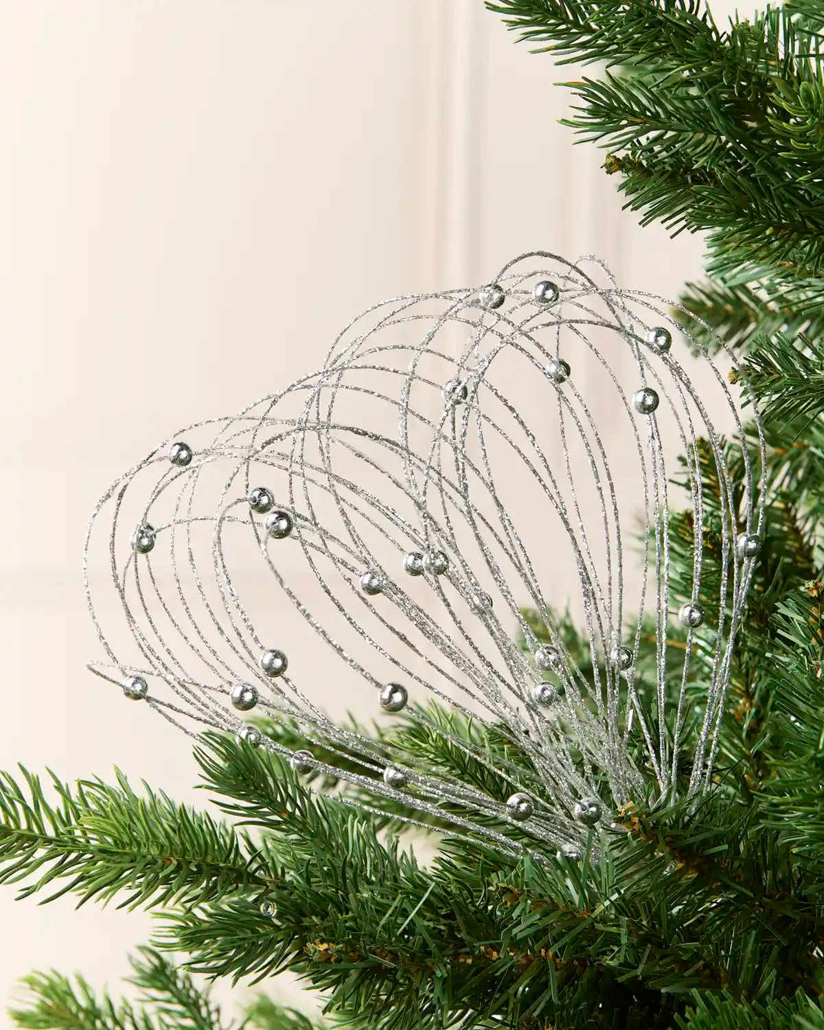 Silver Glitter Nest Christmas Tree Pick placed in green Christmas tree branches with a cream background
