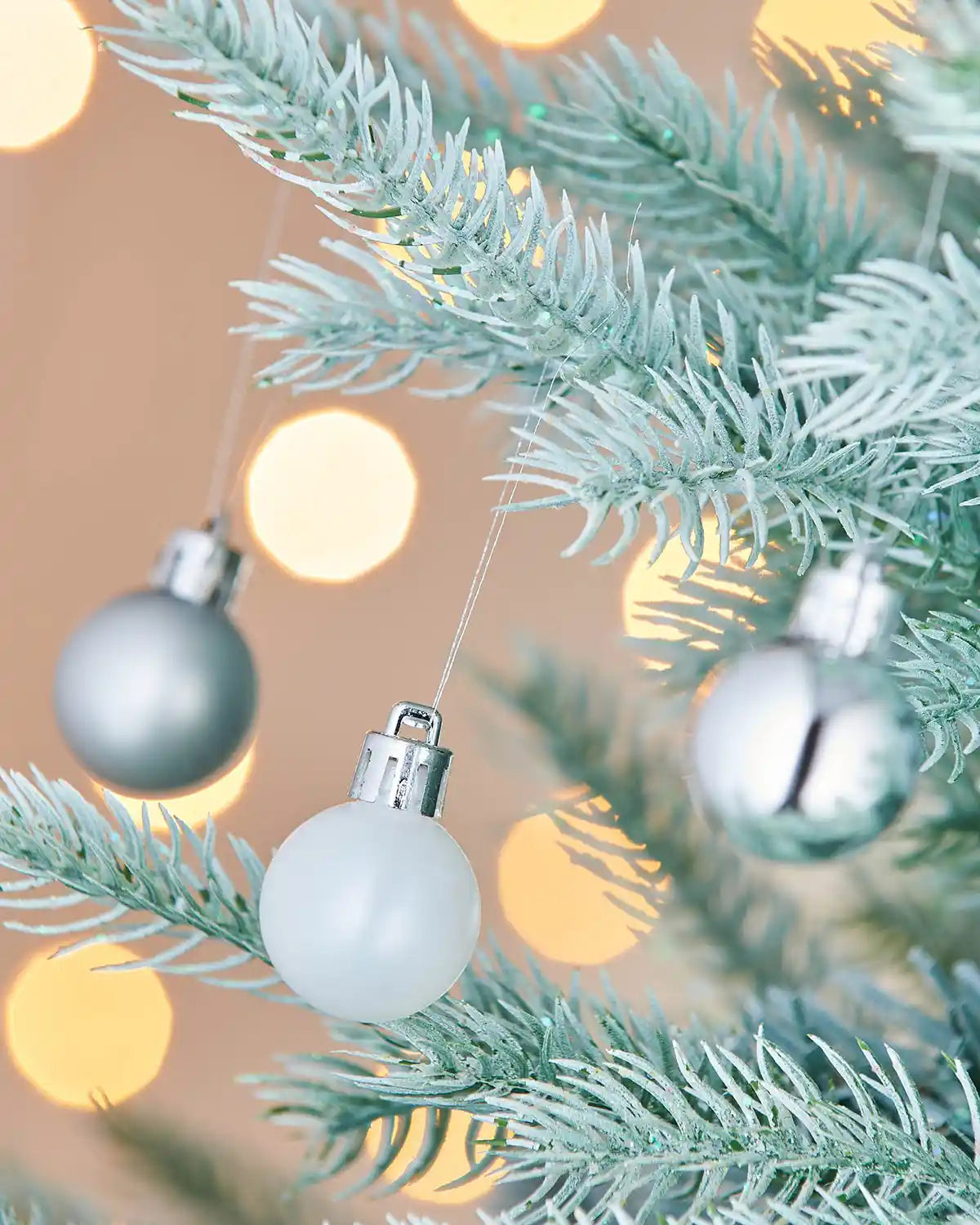 Silver and pearl Christmas baubles on a tree branch with a blurred light background