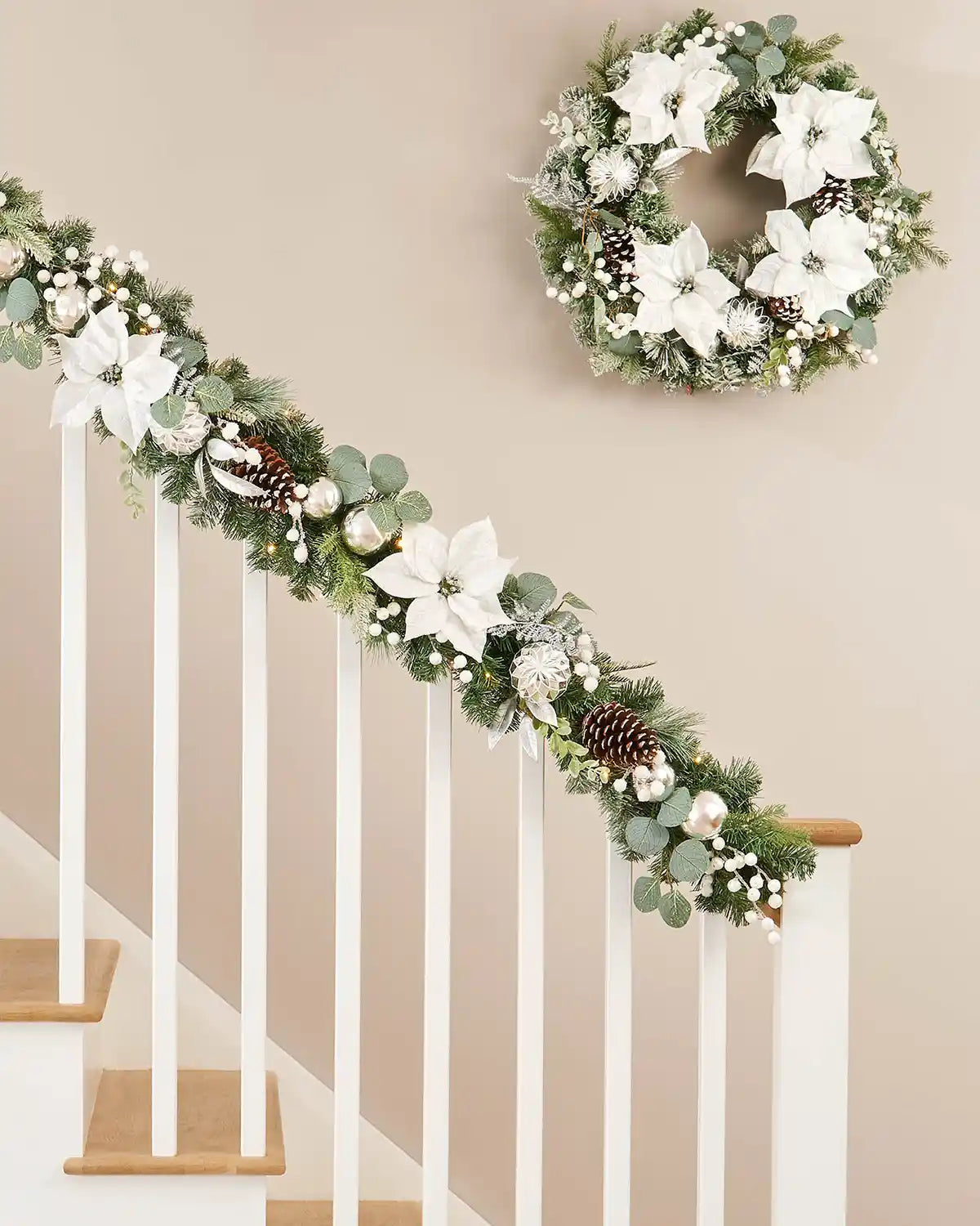 Silver and white garland draped on a white wooden staircase with a matching white and silver wreath hanging above 