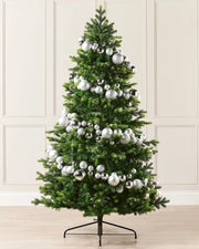 Silver bauble garland wrapped around a Christmas tree against a cream panel wall and a wooden floor 
