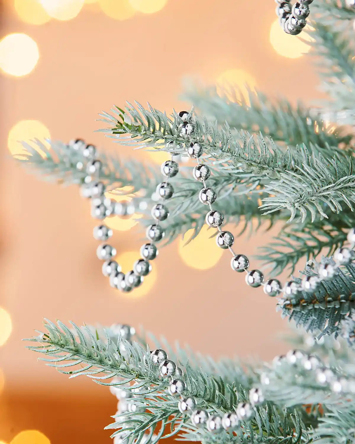 Silver bead garland on a Christmas tree branch with a blurred lights background