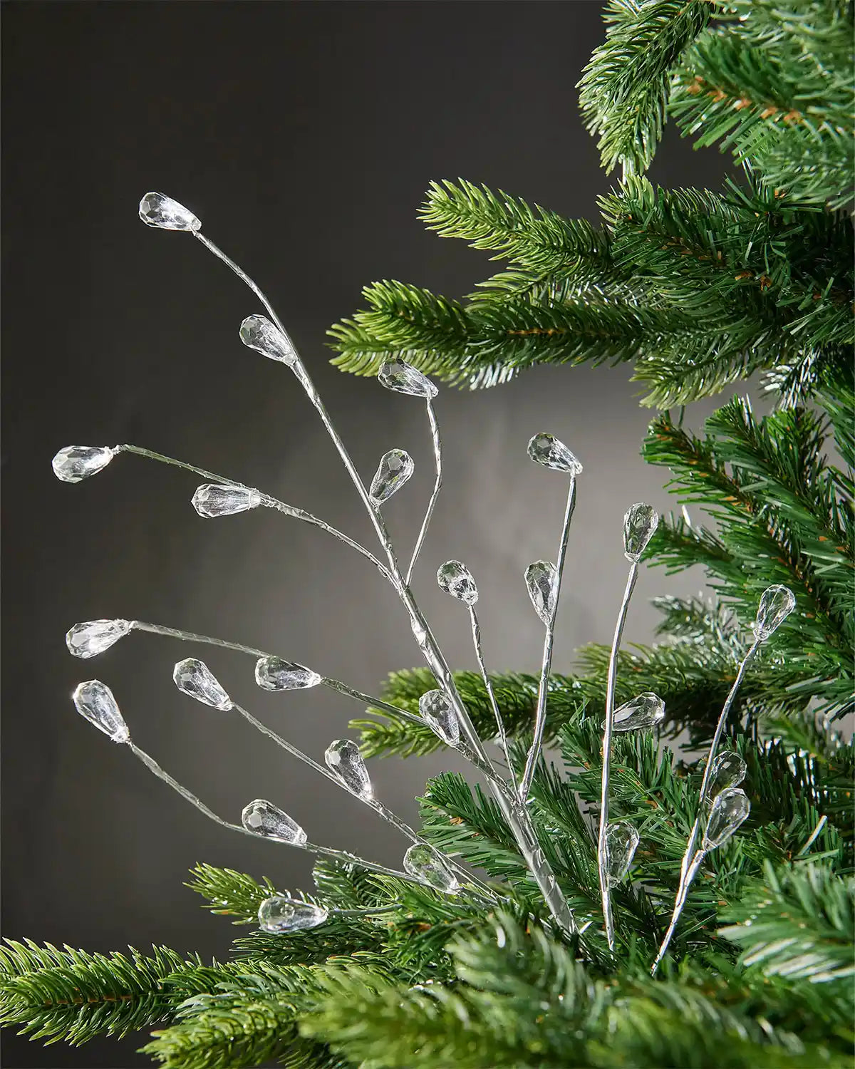 Silver crystal teardrop spray attached to Christmas tree in front of grey wall background