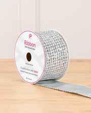 Silver double sided ribbon with sequin squares on a cardboard roll placed on a wooden table against a light background