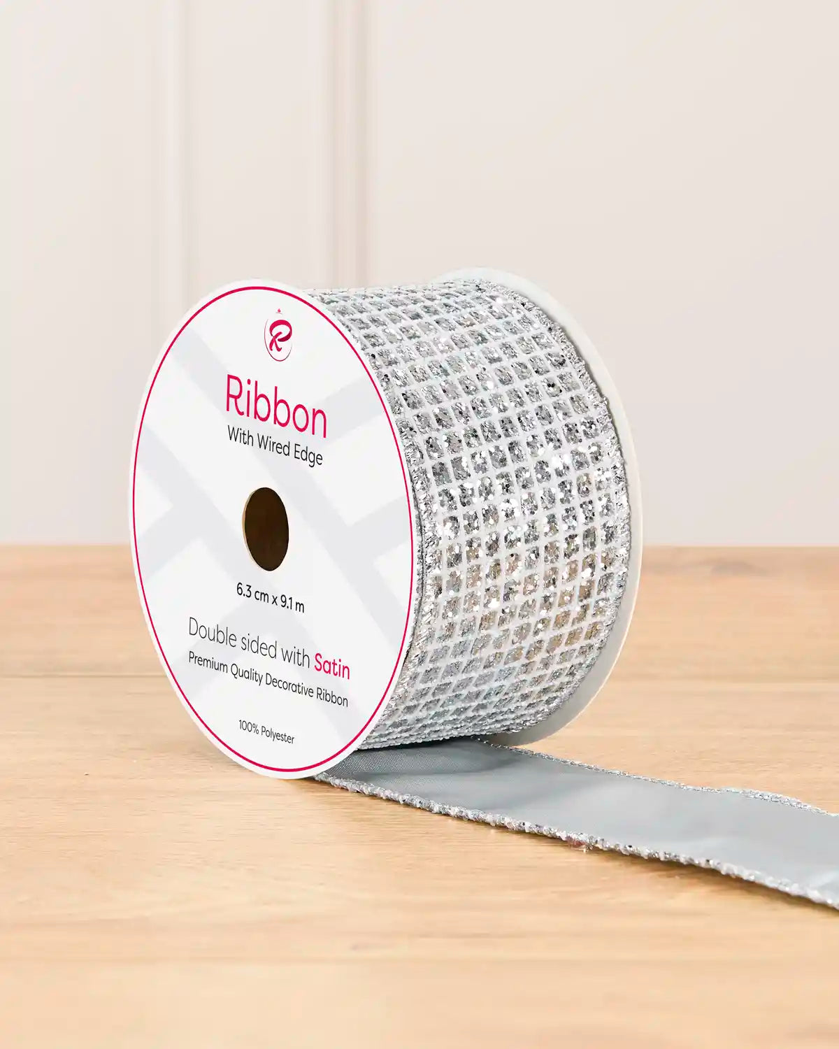 Silver double sided ribbon with sequin squares on a cardboard roll placed on a wooden table against a light background