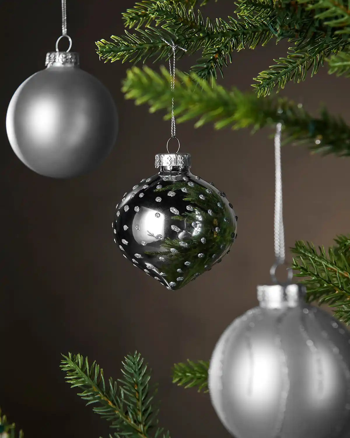 Silver glass baubles hanging on a Christmas tree.