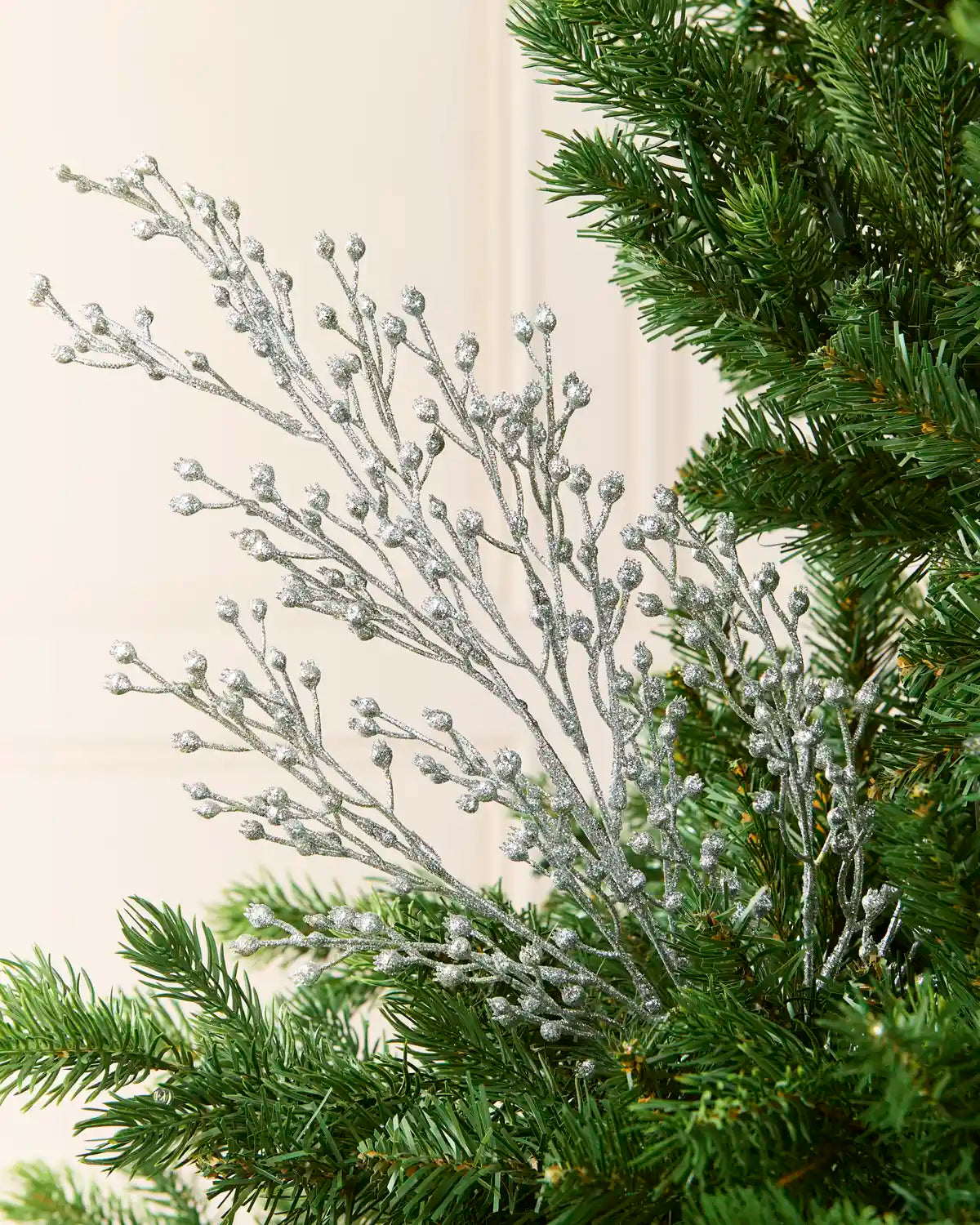 Silver glitter berry Christmas tree spray on a Christmas tree against a cream background