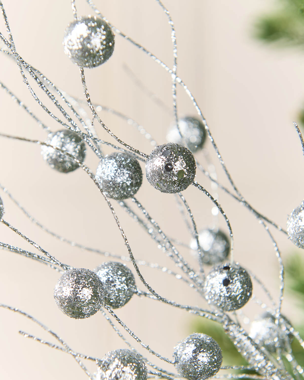 Silver glitter decorative branches with round sparkling ornaments on a soft beige background.