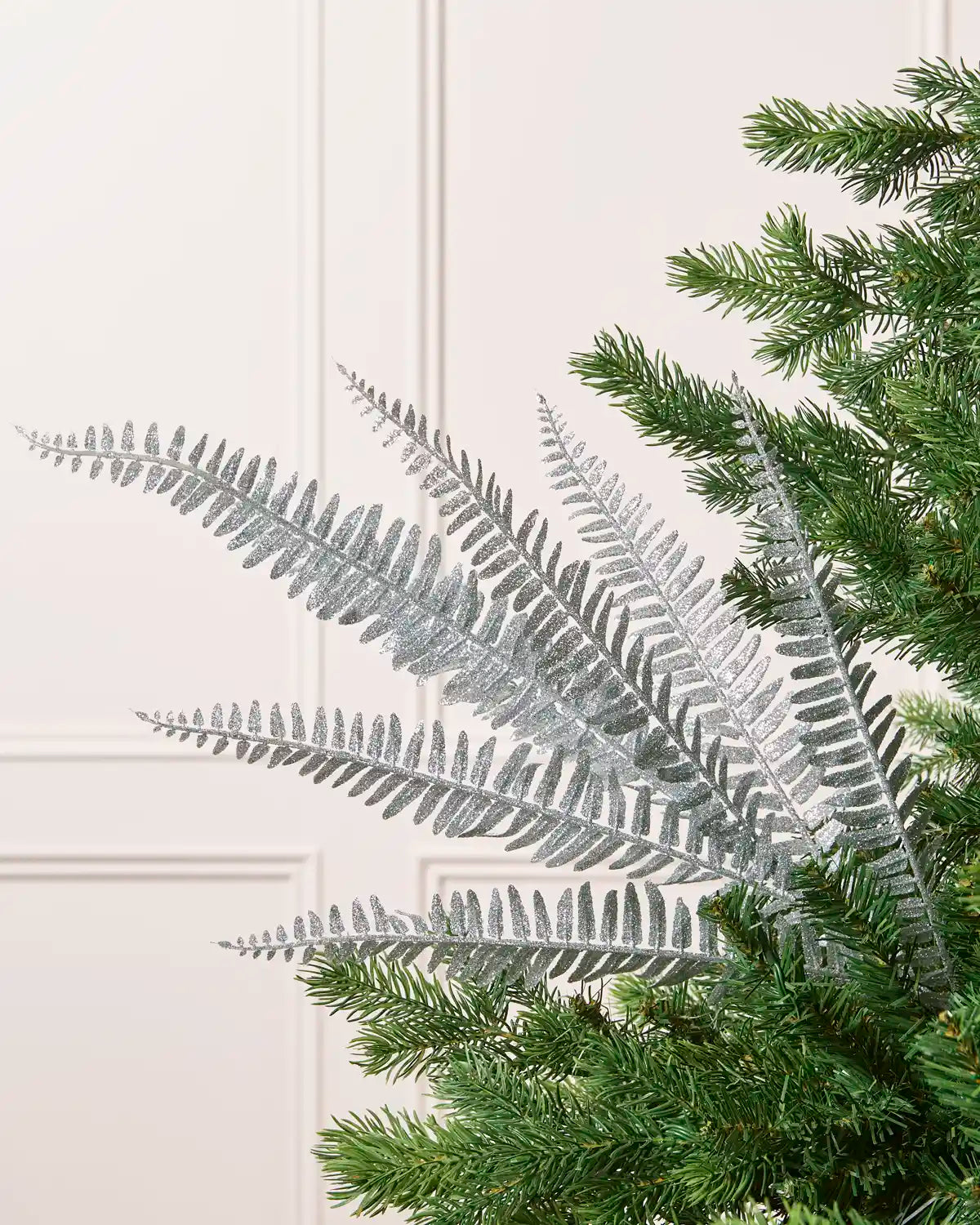 Silver glitter leaf spray displayed with multiple glitter-covered branches against a cream background and Christmas tree branches