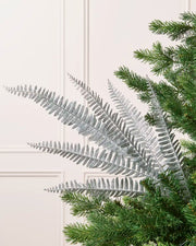 Silver glitter leaf spray displayed with multiple glitter-covered branches against a cream background and Christmas tree branches