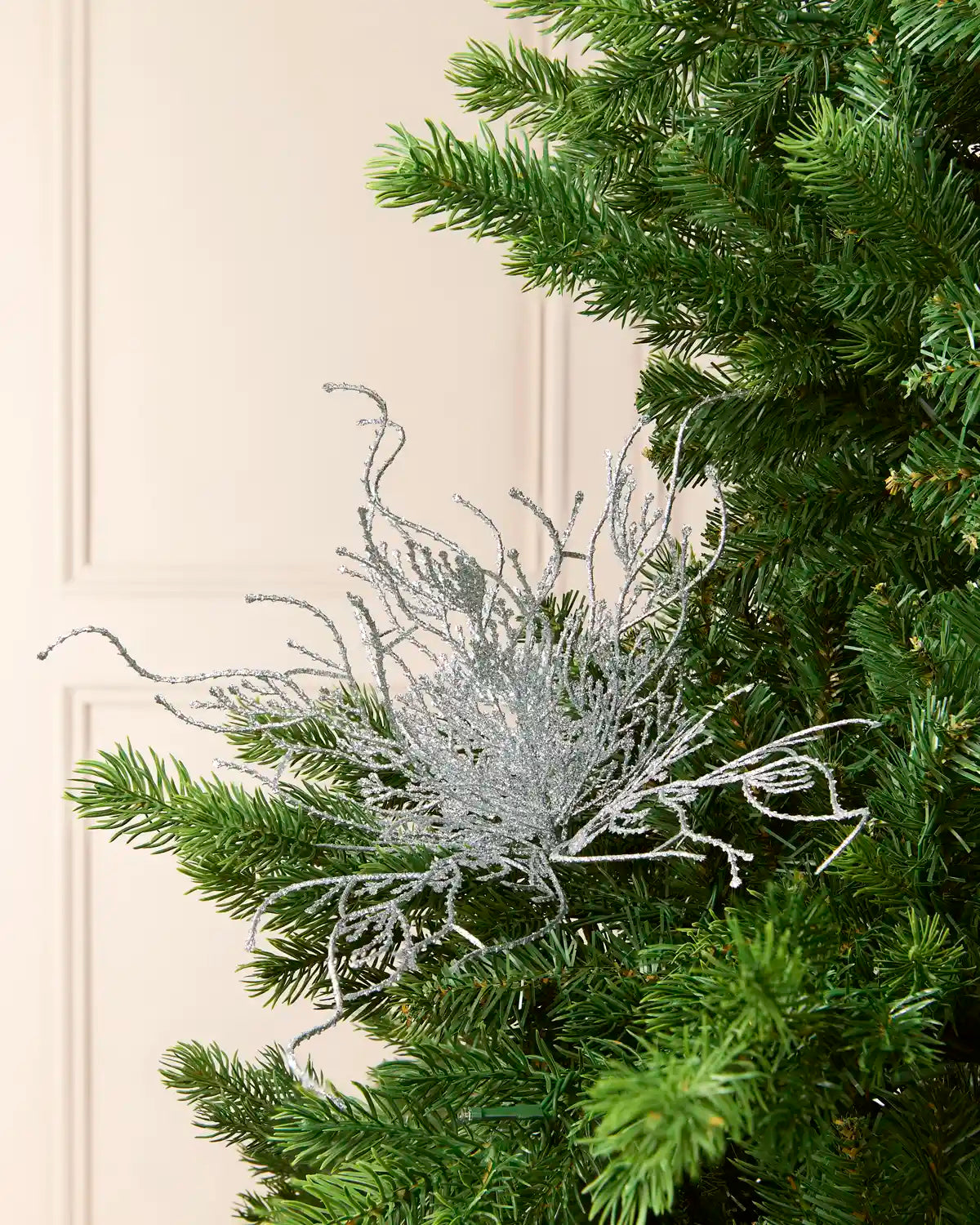Silver glitter twig style Christmas tree pick on a Christmas tree branch against a cream background