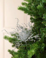 Silver glitter twig style Christmas tree pick on a Christmas tree branch against a cream background