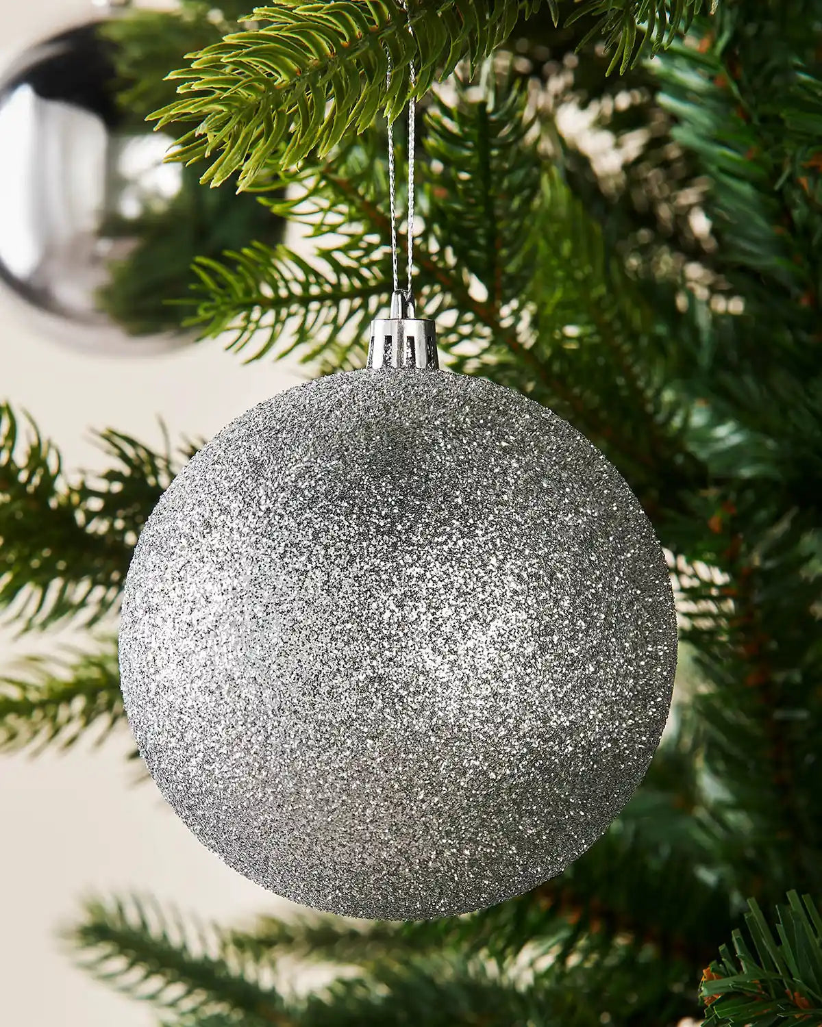 Silver glittery Christmas ball ornament hanging on a tree branch