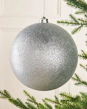 Silver glittery Christmas bauble hanging on a tree branch.