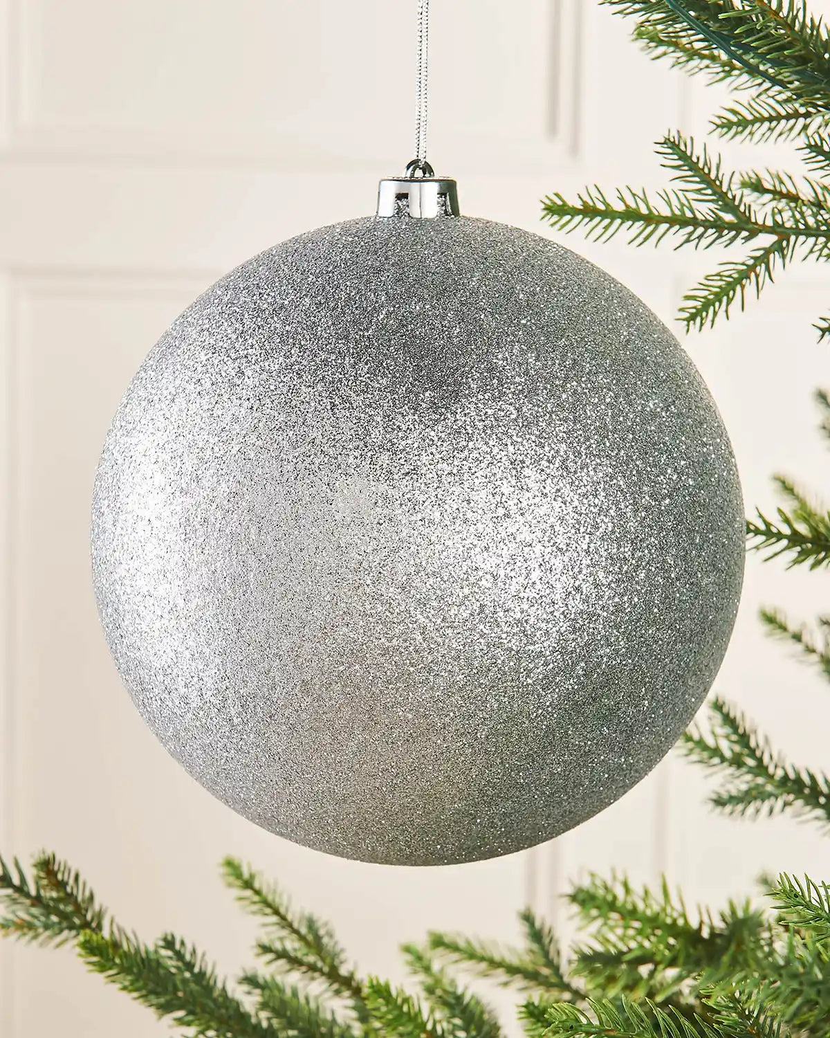 Silver glittery Christmas bauble hanging on a tree branch.