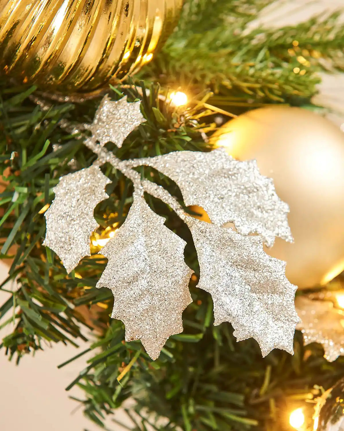 Silver glittery Holly leaves on a Christmas garland with lights and gold ball.