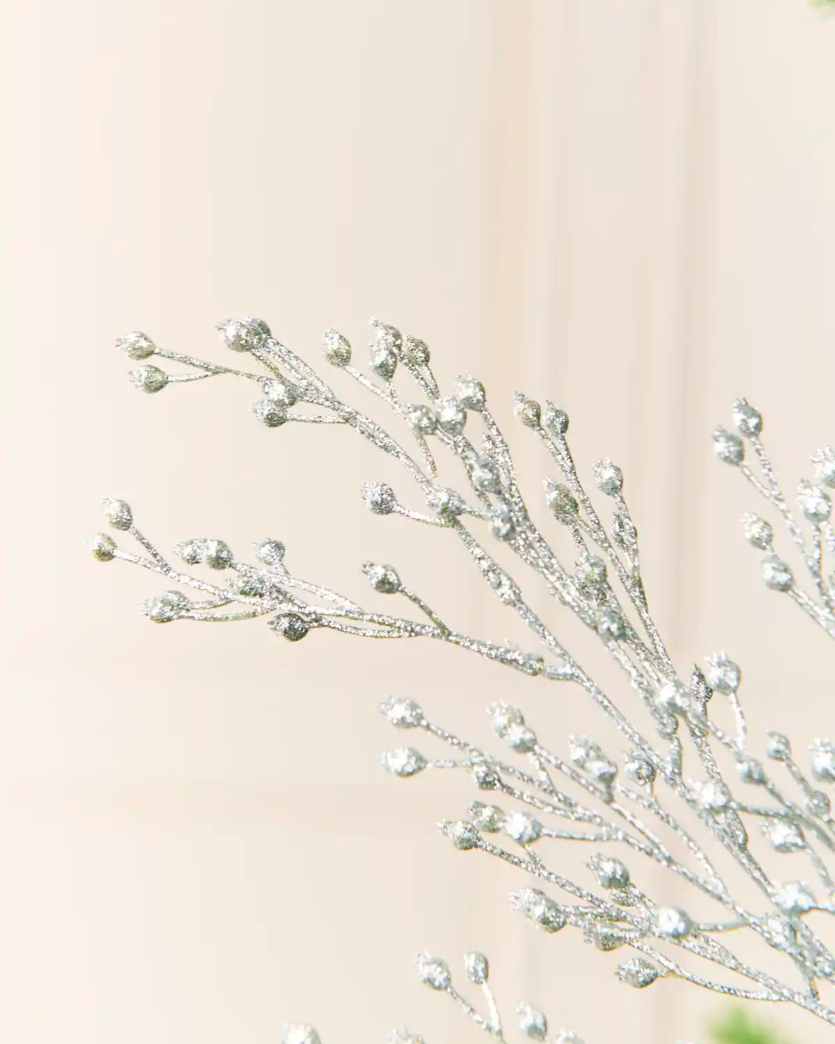 Silver glittery decorative spray ornament with frosted buds, shown close-up against a light neutral background.