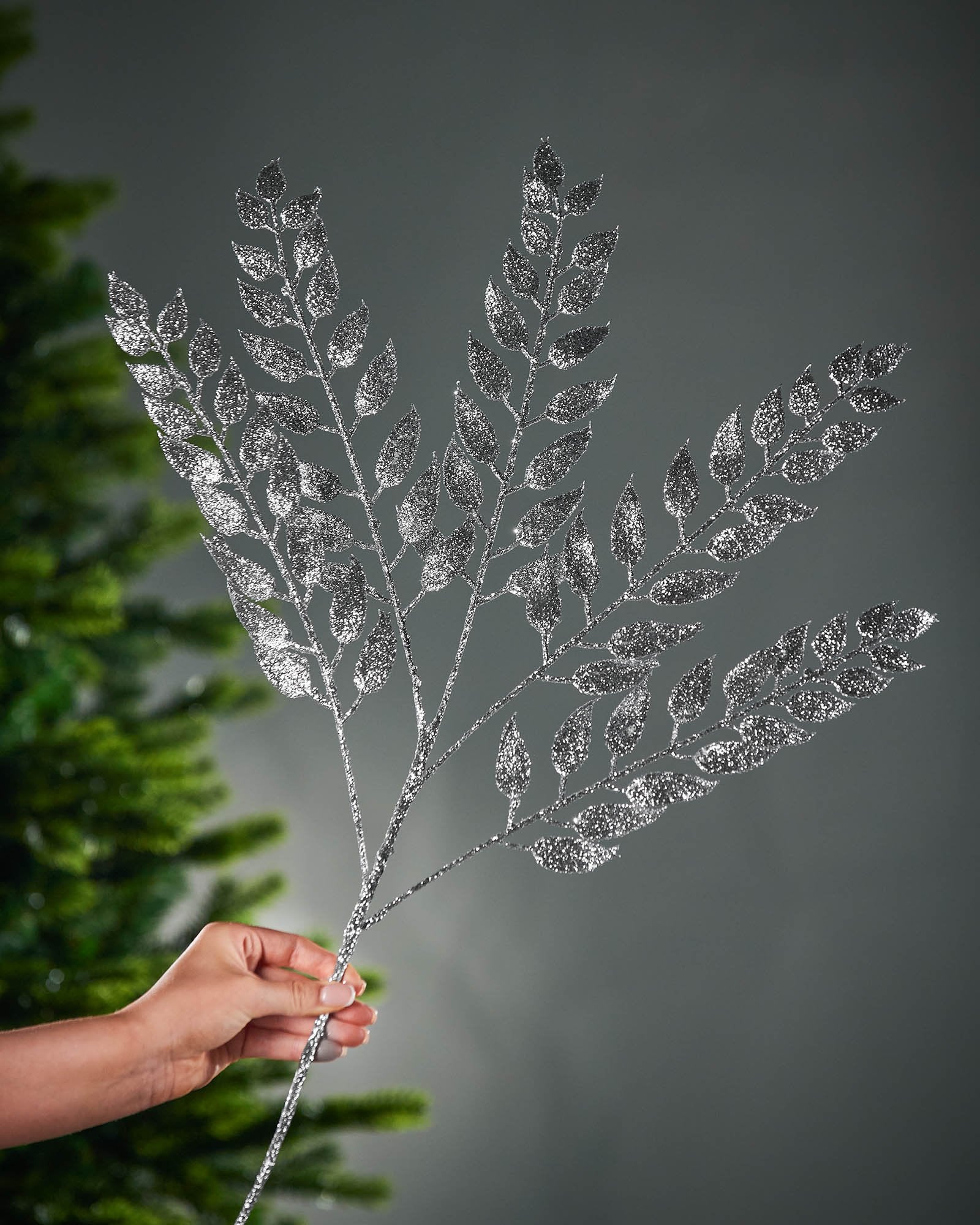 Silver glittery leaf branch held by a hand against a dark background