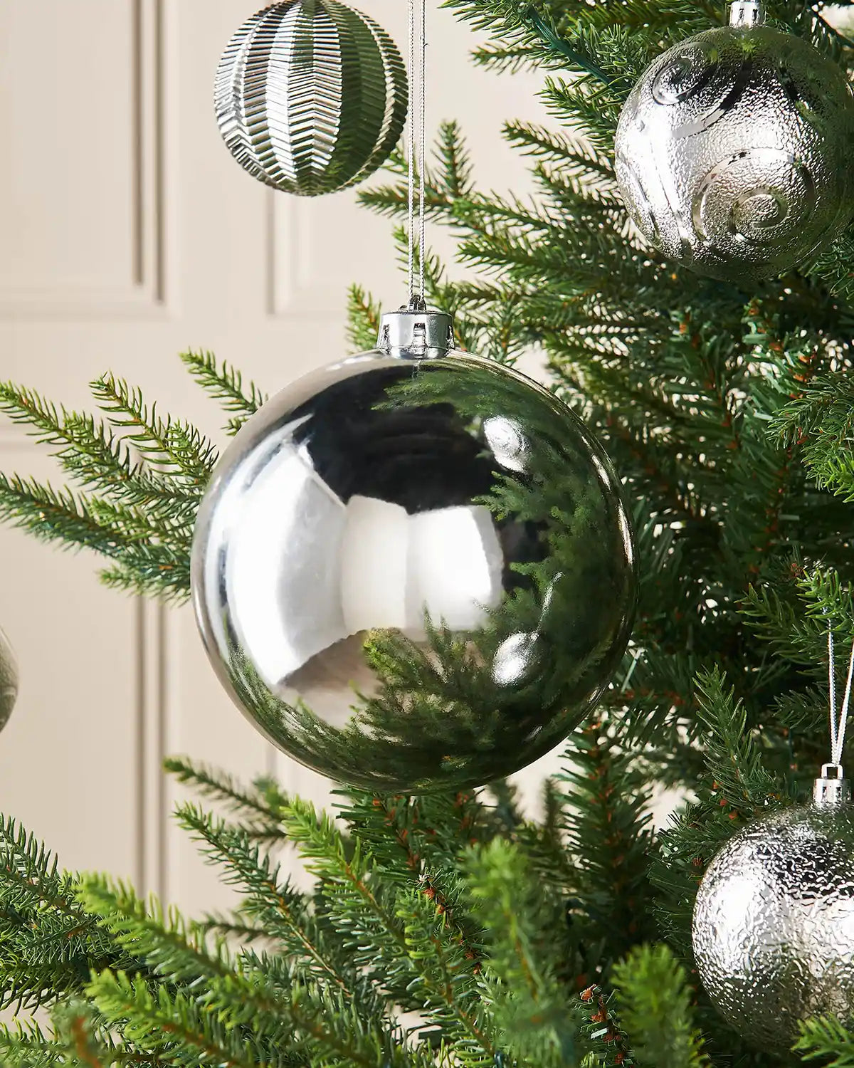 Silver gloss 15cm oversized bauble on a Christmas tree branch with 4 smaller silver baubles in background