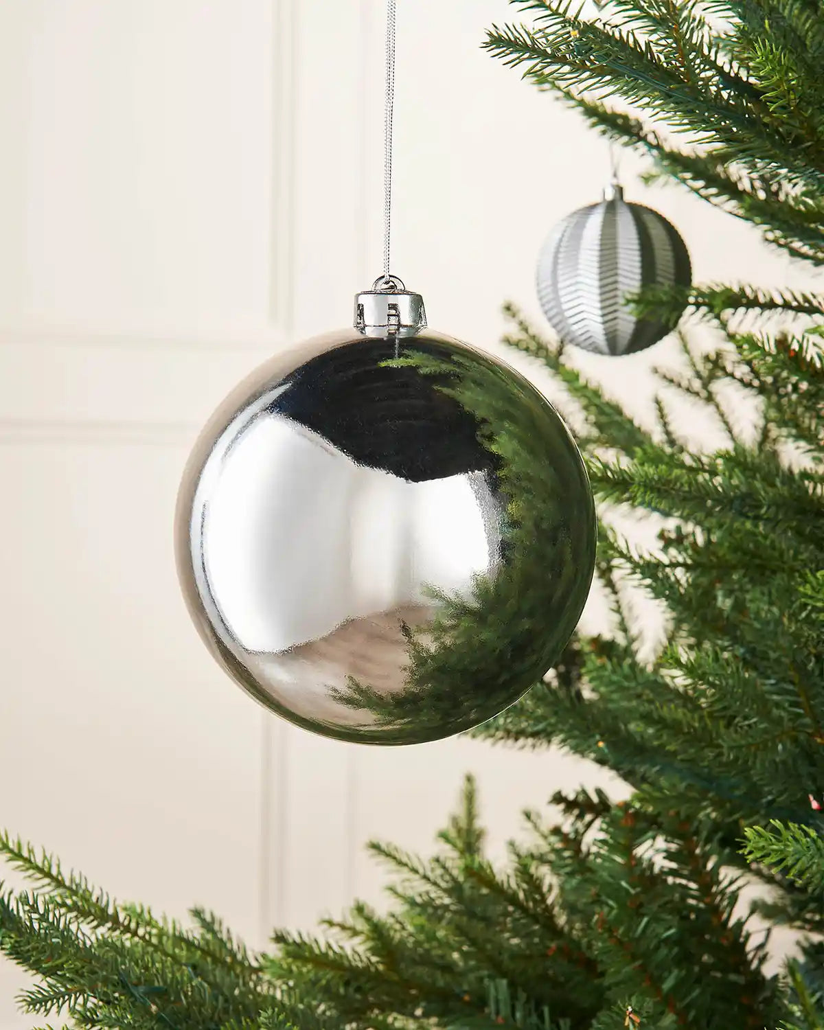 Silver gloss 15cm oversized bauble on a Christmas tree branch with a smaller silver bauble in background