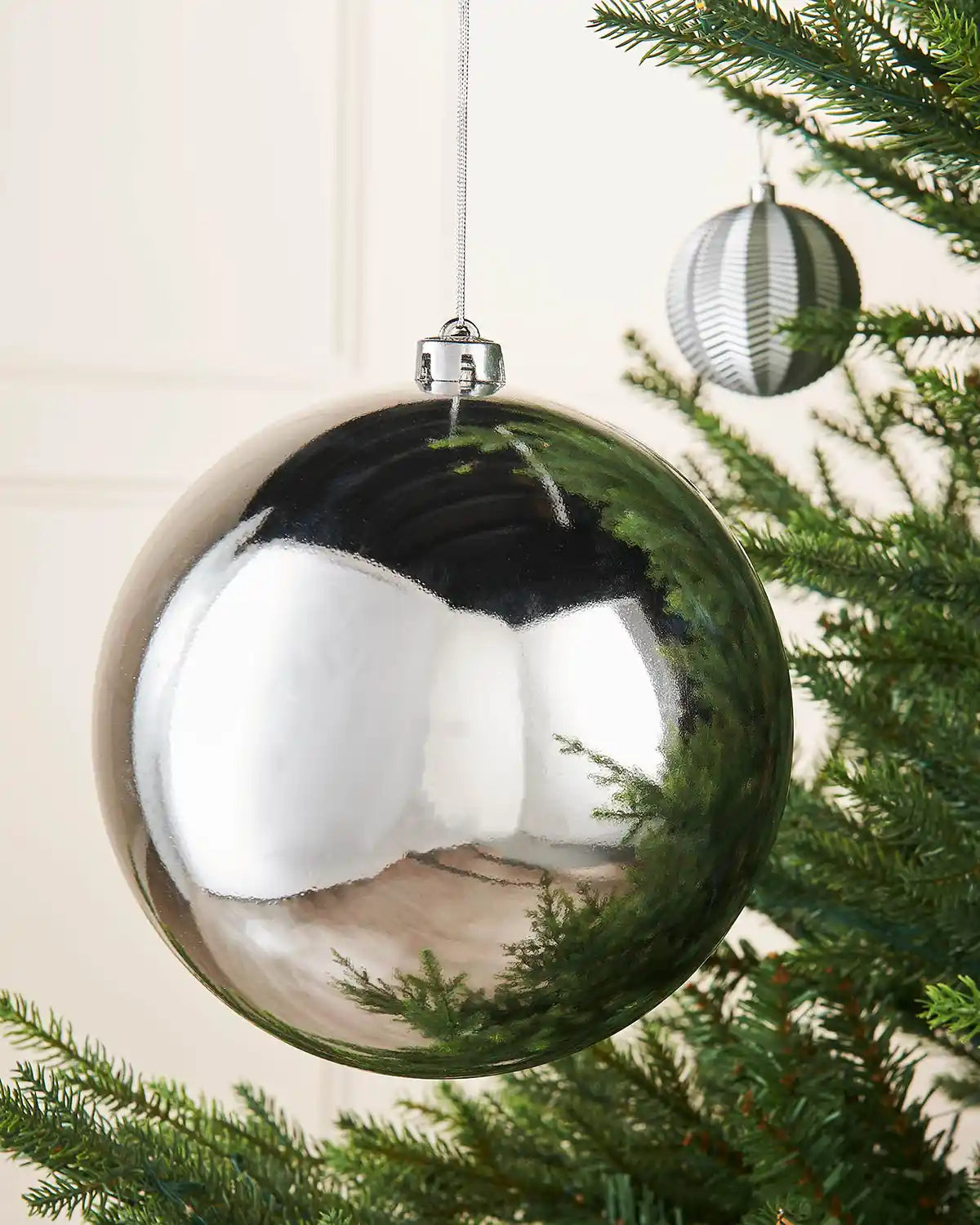 Silver gloss oversized bauble on a Christmas tree branch accompanied by a smaller silver bauble