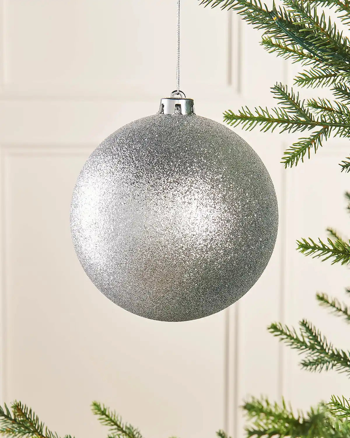 Silver oversized 15cm glitter bauble on a Christmas tree branch