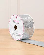 Silver sequin double sided wire edge ribbon in a cardboard roll on a wooden table against a light background