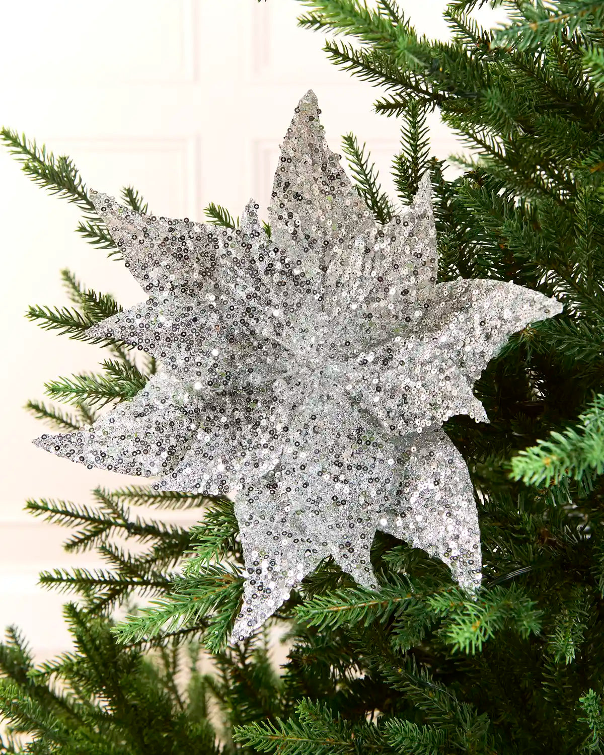 Silver sequin poinsettia on Christmas tree against a light background 