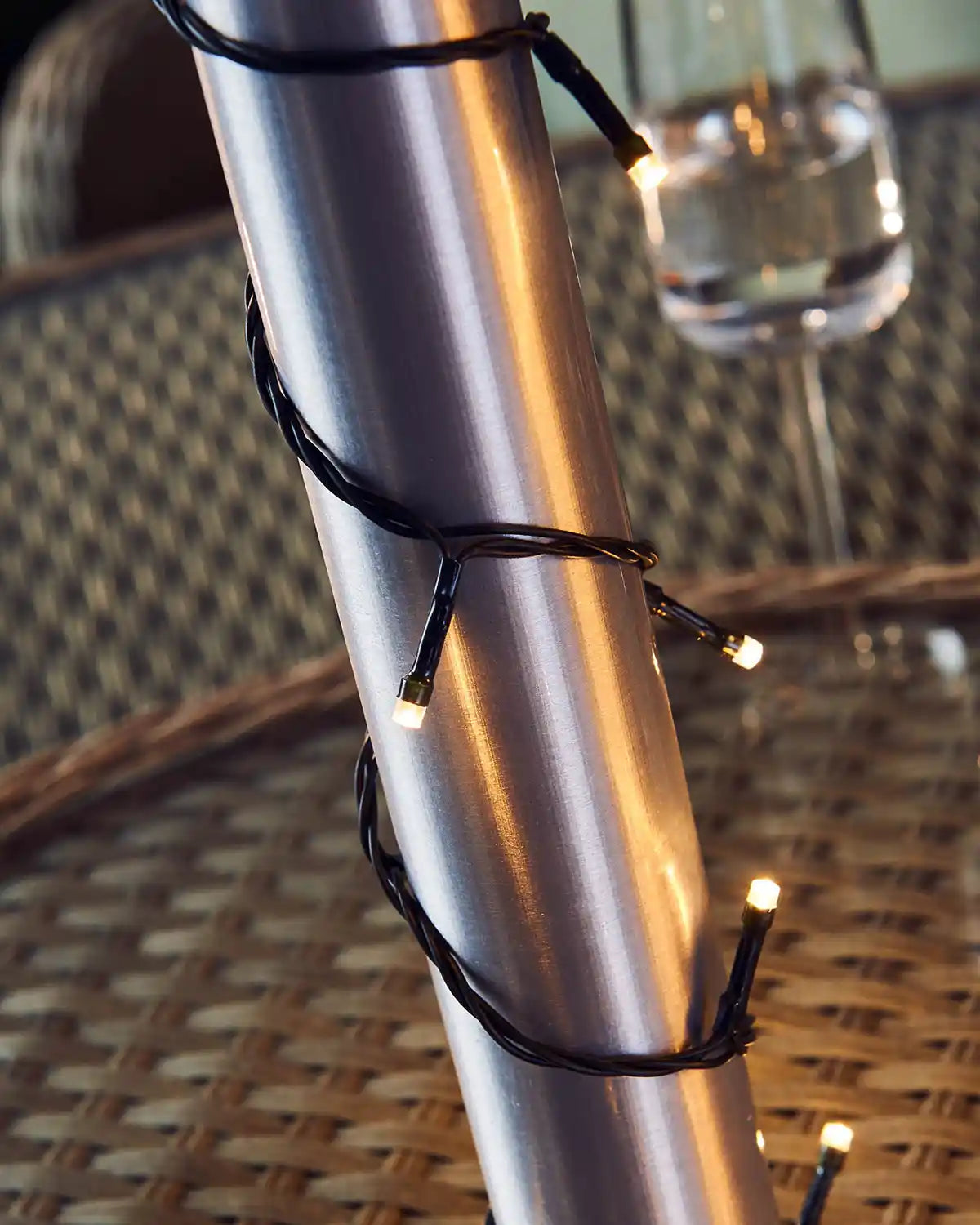 Silver umbrella pole with warm white string lights on a wicker surface