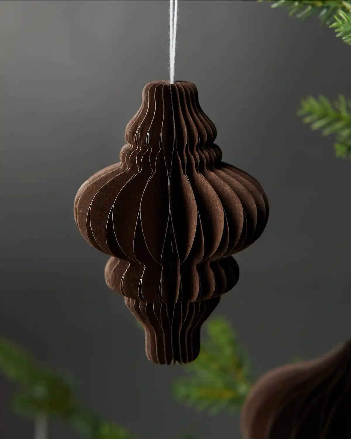 Image of a single 10cm espresso brown paper honeycomb tree decoration hanging on Christmas tree in front of grey wall background