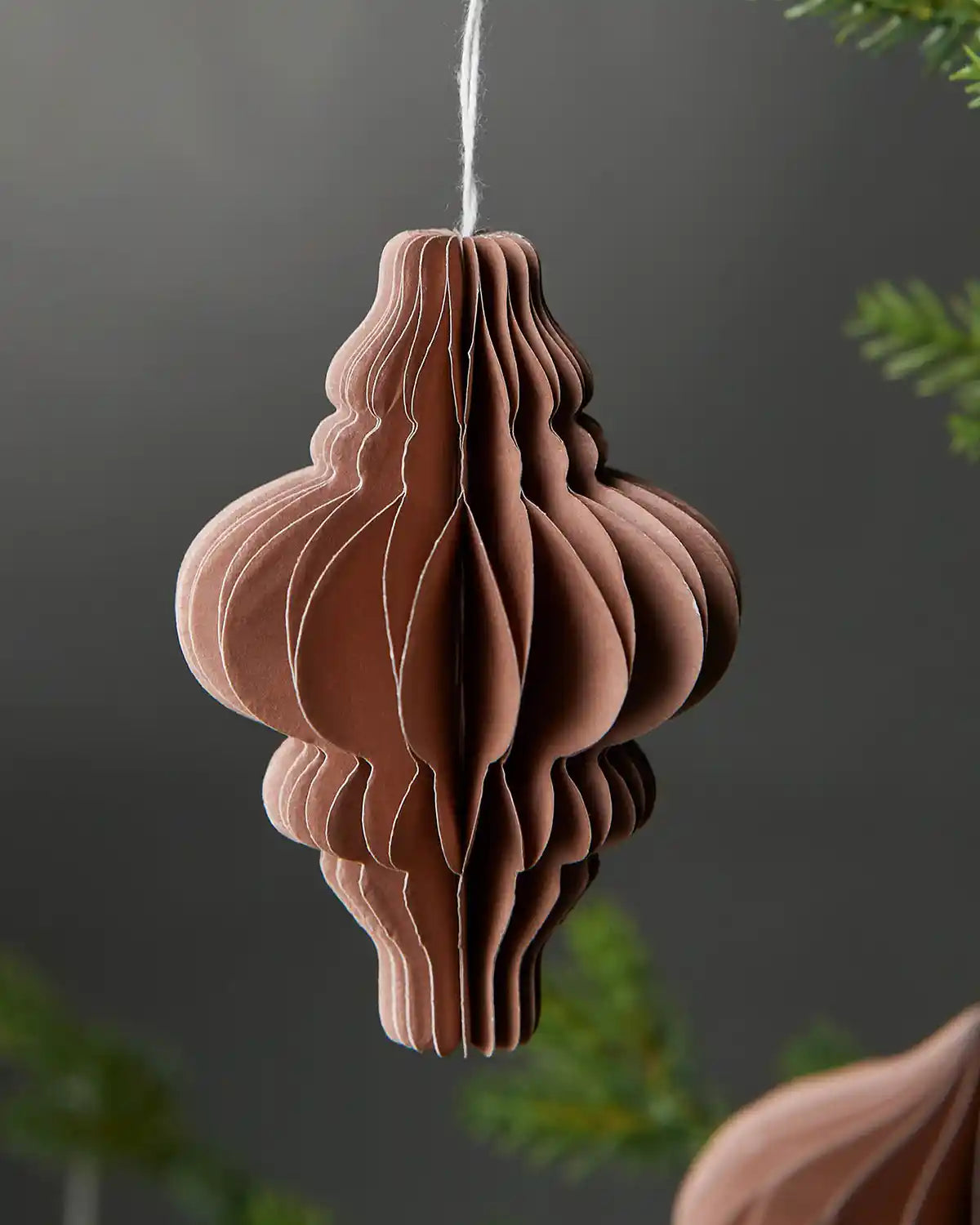 Image of single 10cm mocha brown paper Christmas decoration hanging on tree in front of grey wall background