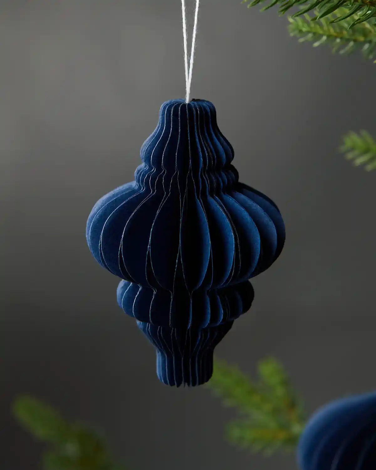 Single 10cm navy blue paper honeycomb Christmas tree decoration hanging on tree in front of grey background