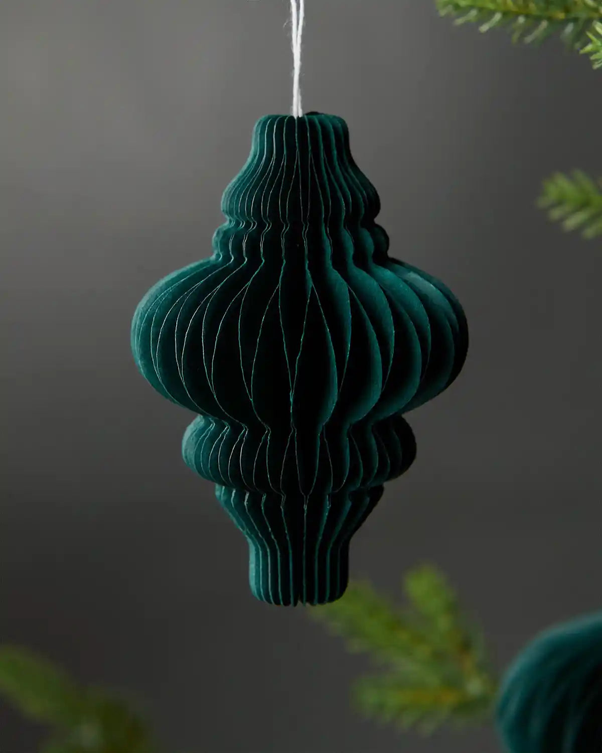 A single 10cm sage green paper honeycomb tree decoration hanging on Christmas tree in front of grey wall background