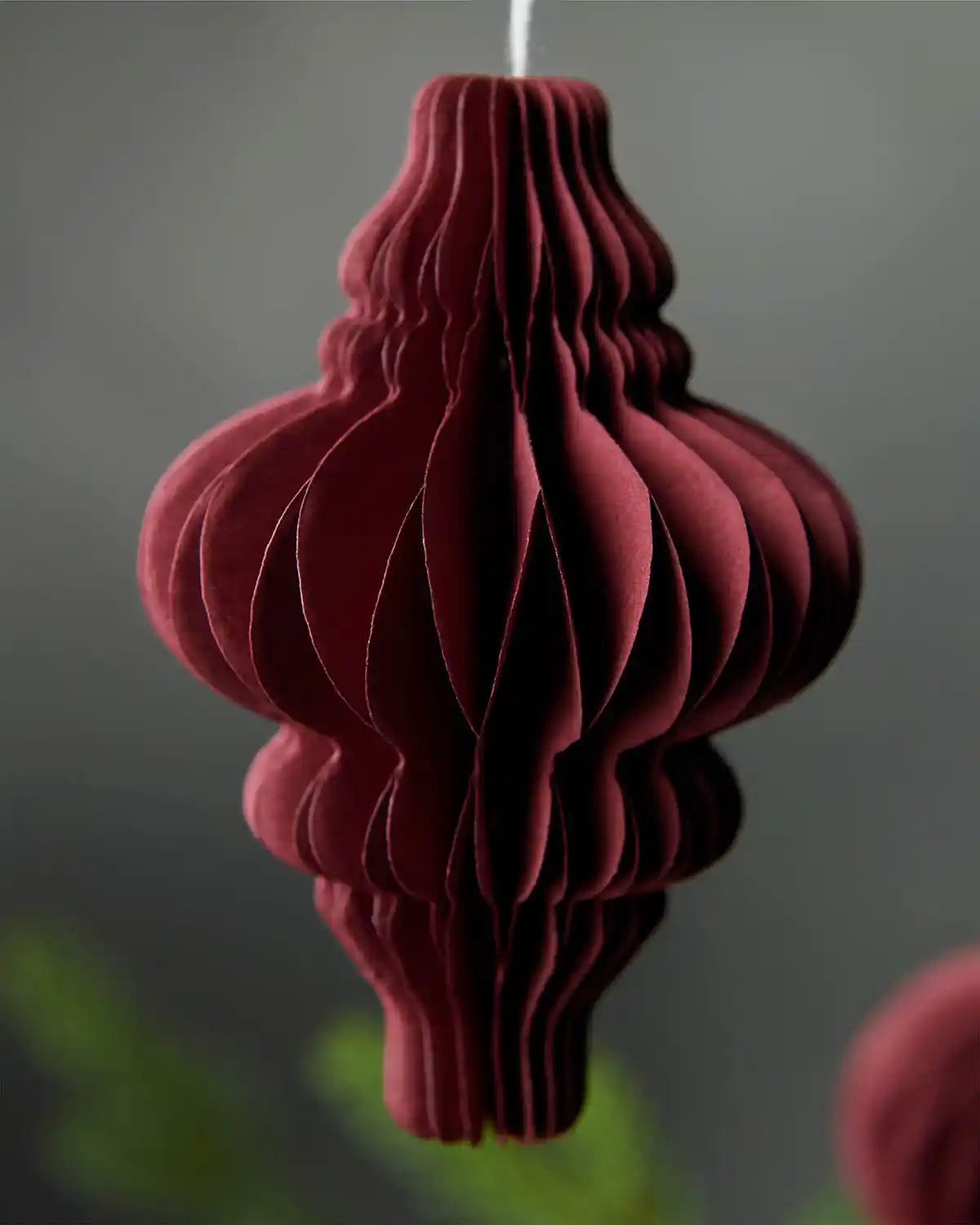 Close-up of a single burgundy paper Christmas tree hanging decoration in front of blurred grey background