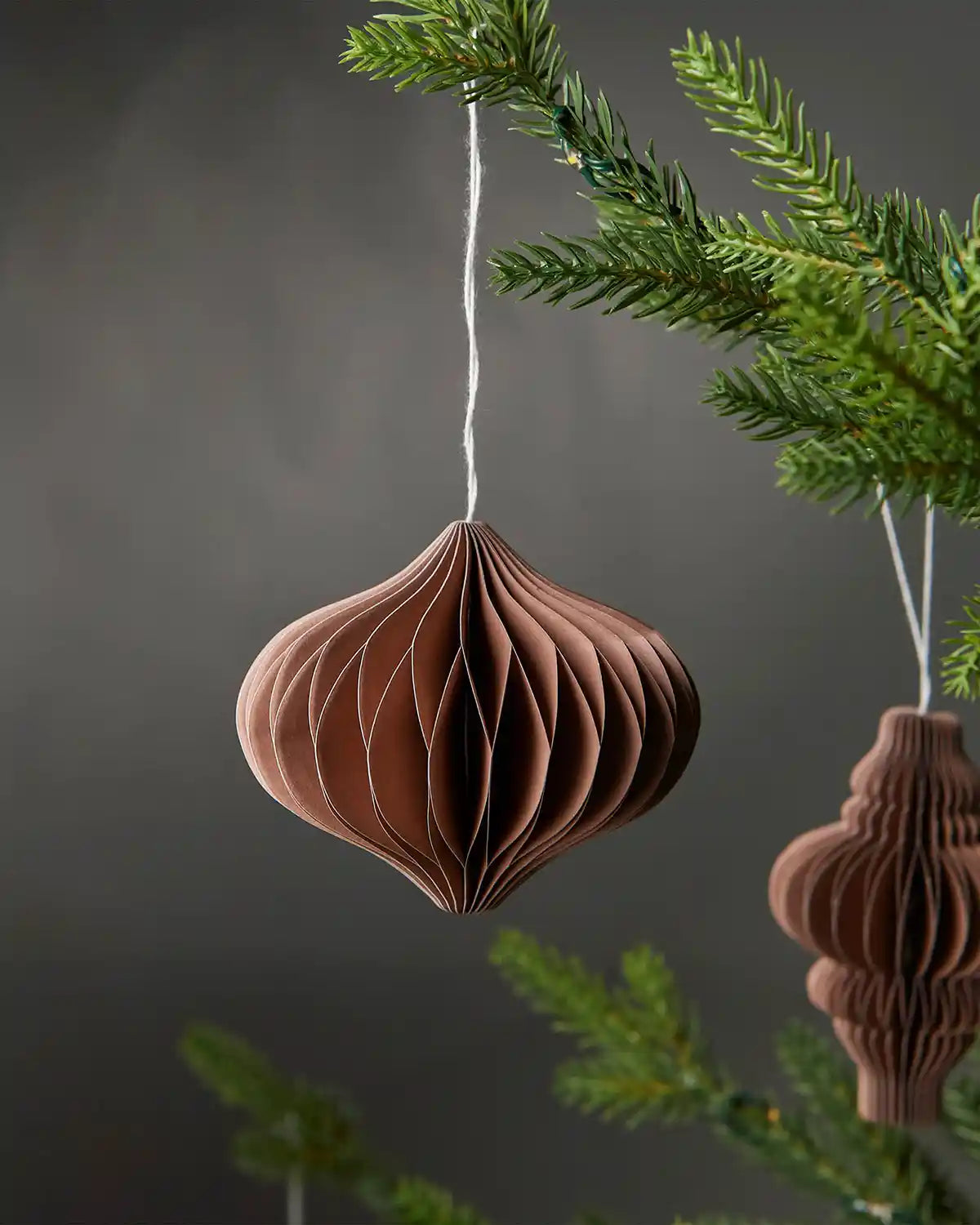 Single bulb-shaped mocha brown Christmas decoration hanging on a tree in front of a grey wall background