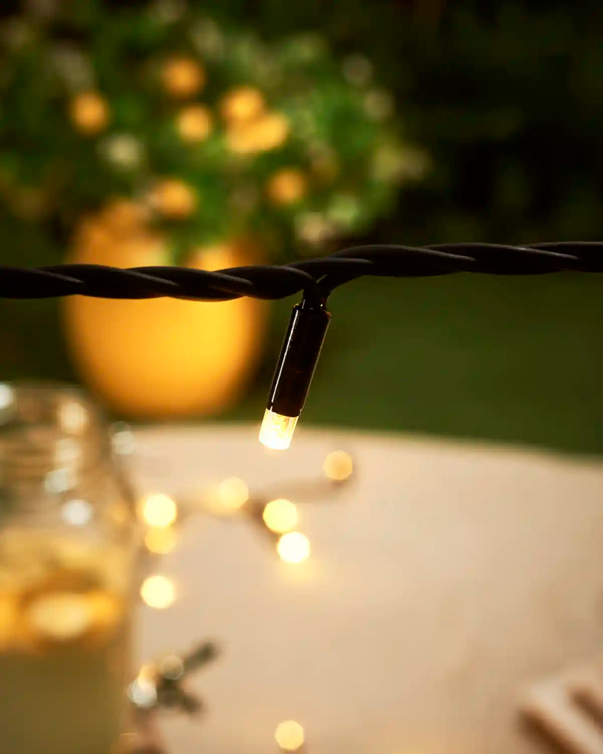 Singular warm white LED facing downwards, with a blurry yellow plant pot and blurry garden in the background.