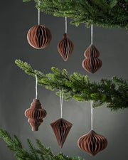 Six 10am mocha brown paper Christmas decorations hanging on Christmas tree branches in front of a grey wall background