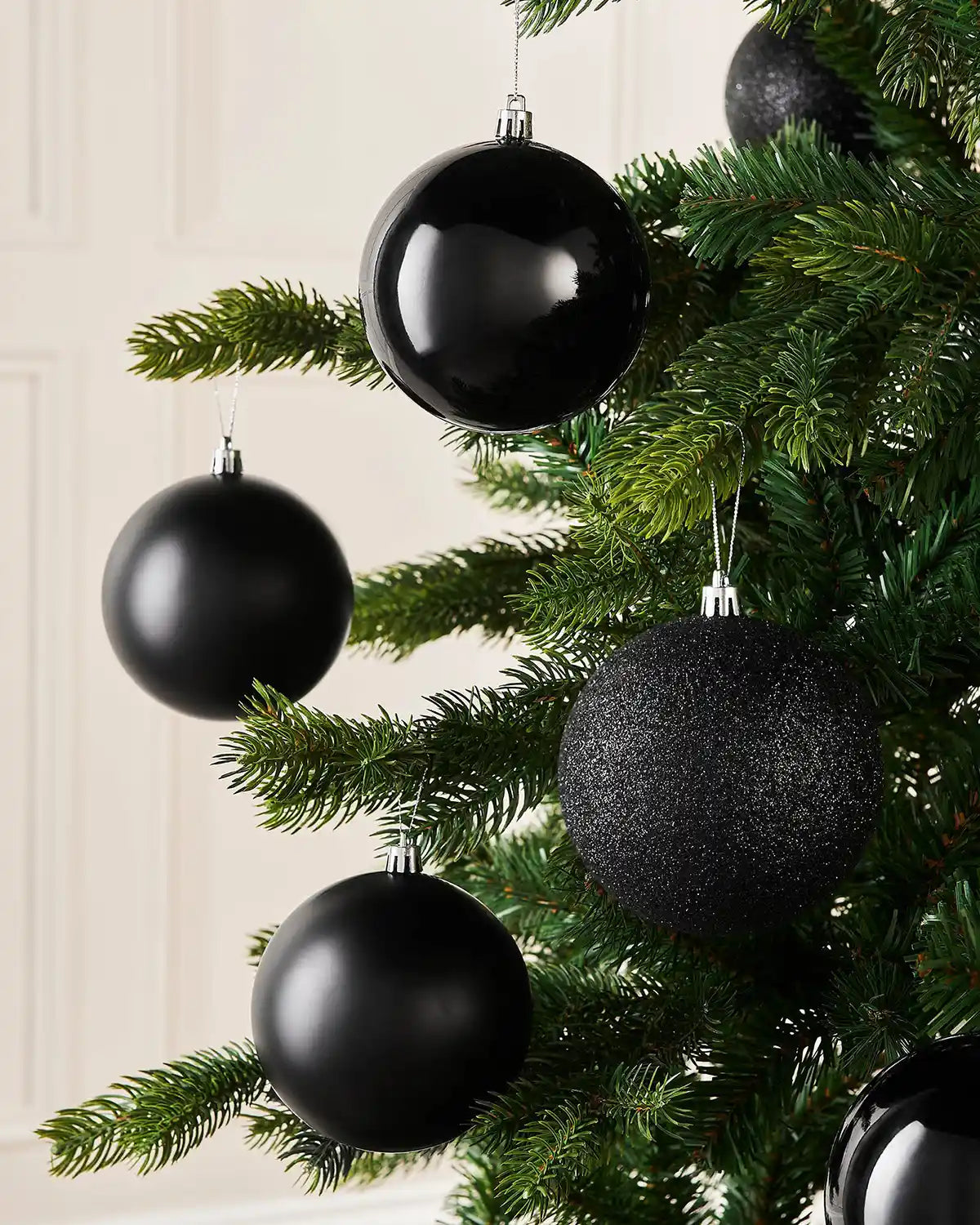 Six Black baubles hanging on a Christmas tree against a cream panel wall