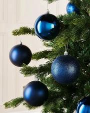 Six blue Christmas baubles on a Christmas tree against a white wall