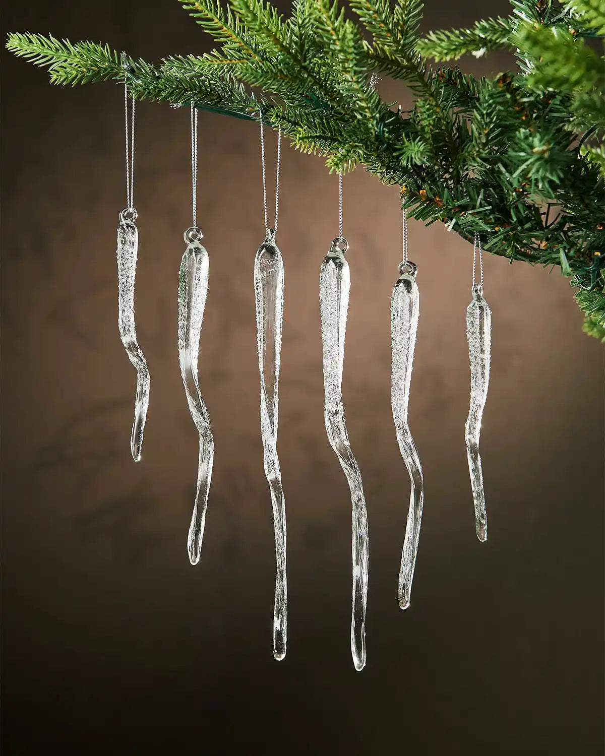 Six frosted glass crystal hanging ornaments on a Christmas tree branch against a brown background