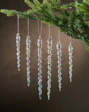 Six iridescent crystal icicle ornaments hanging from a Christmas tree branch against a brown background  