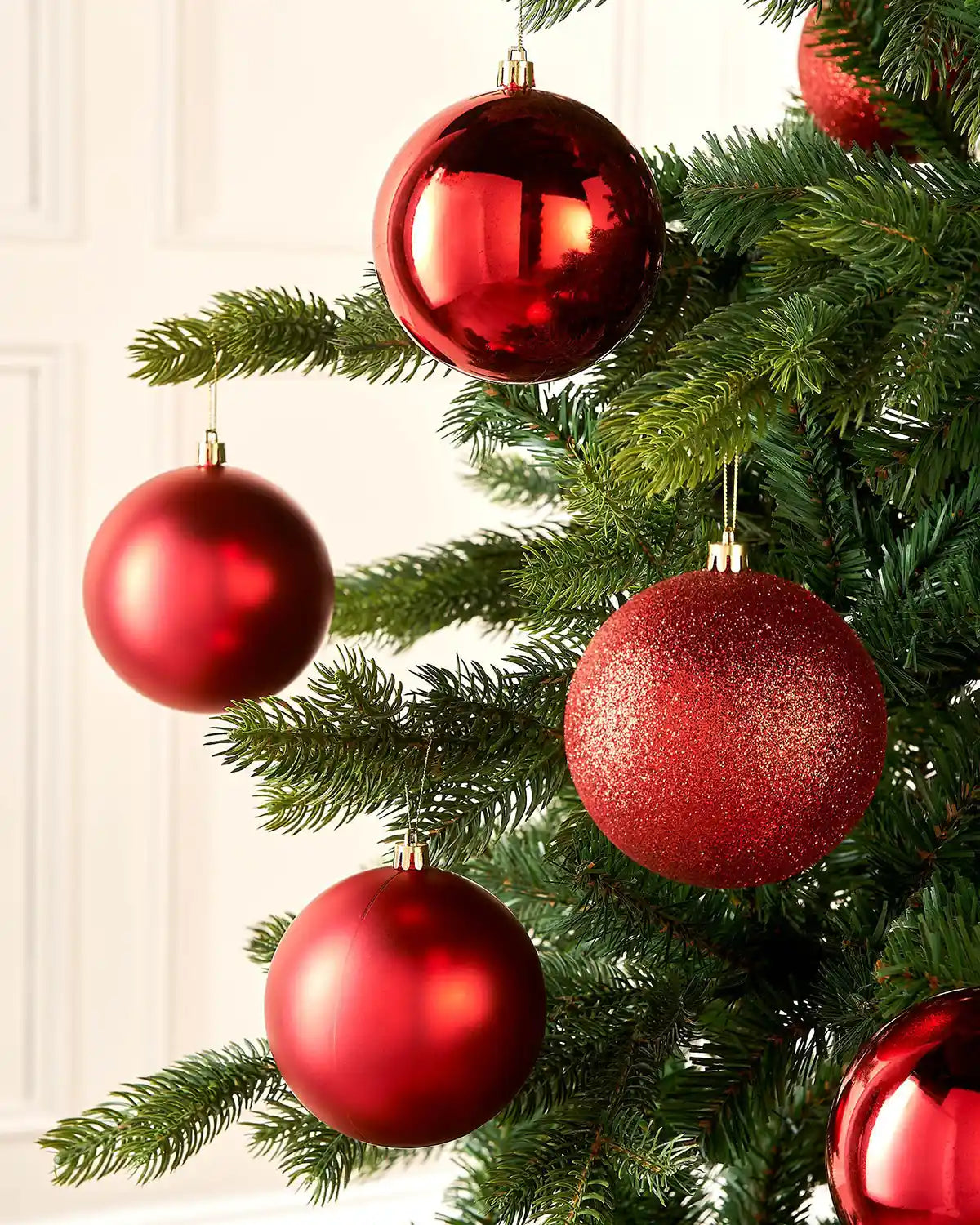 Six red mixture of textured baubles on a Christmas tree against a cream panel wall