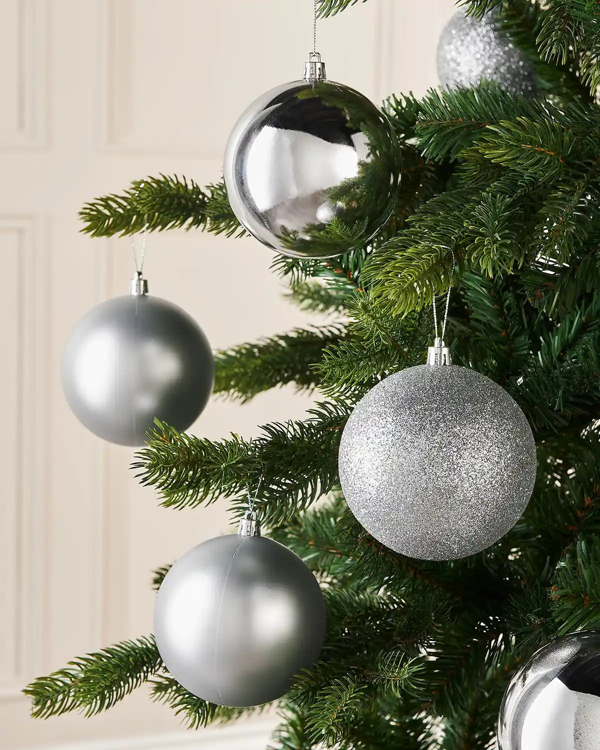 Six silver Christmas baubles on a Christmas tree against a cream wall