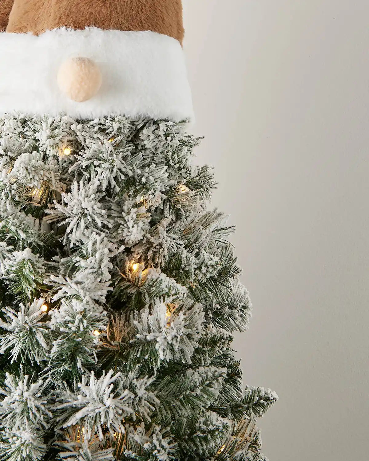 Small gonk side view Christmas tree with Brown Santa hat and brown boots against a white wall on a wooden table