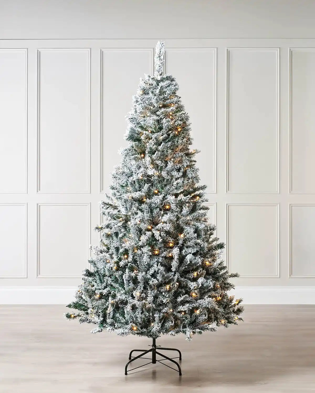 Snow Flocked Mixed Pine Christmas Tree, 6 ft with warm white lights against a cream panel wall