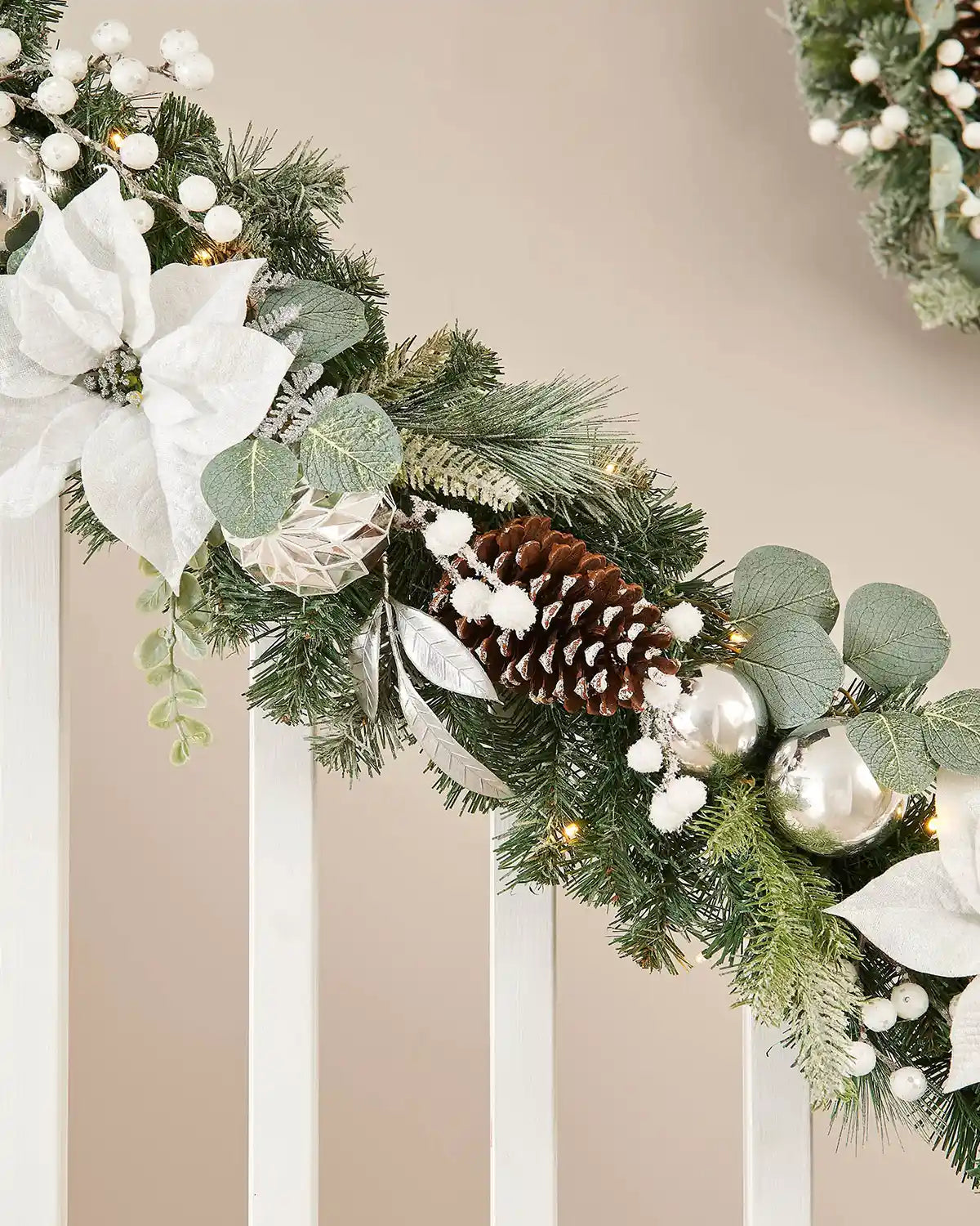 Silver and white garland with snow-covered flora and foliage on white wooden staircase banister