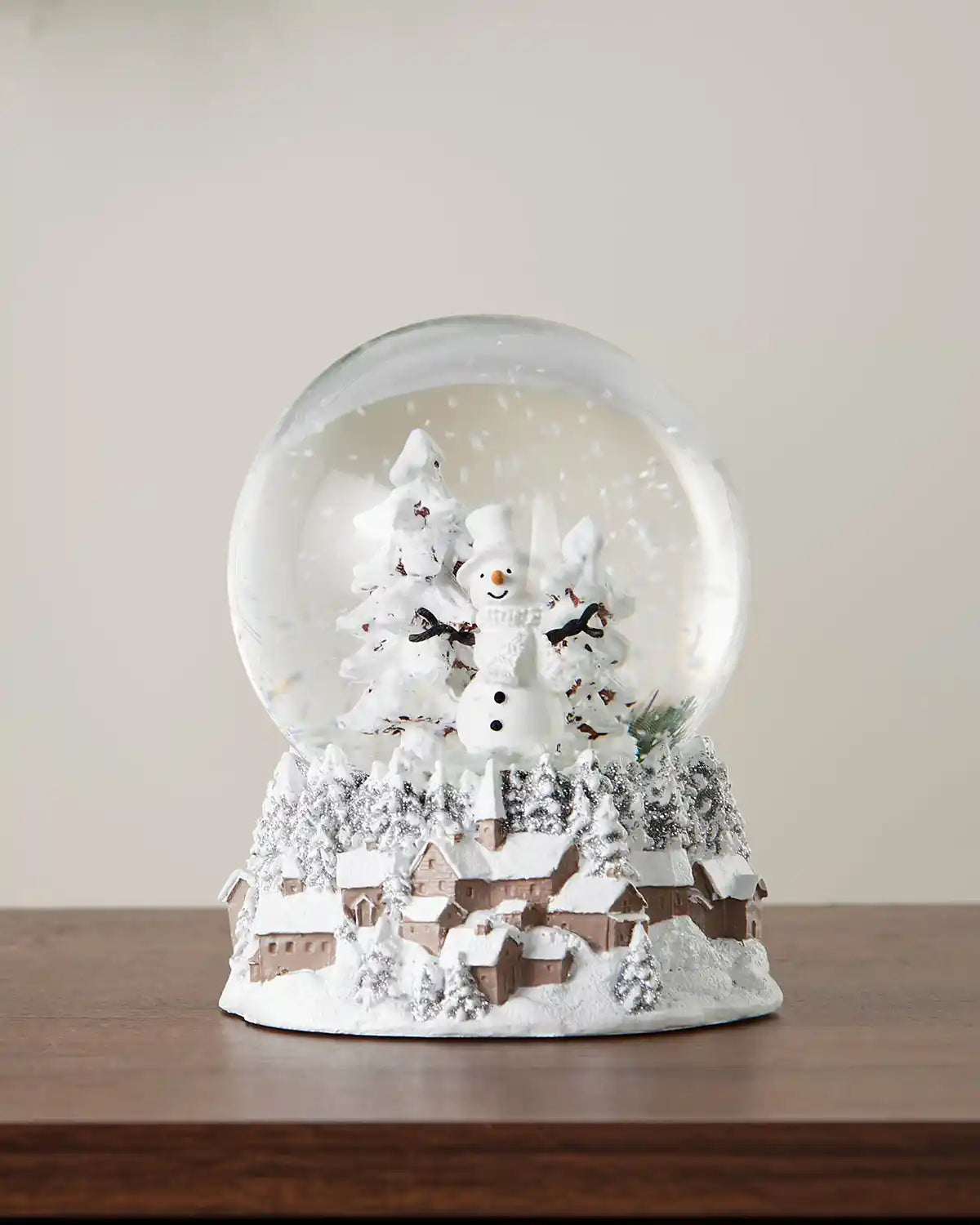 Full image of snowman snow globe on dark wood surface in front of white wall background