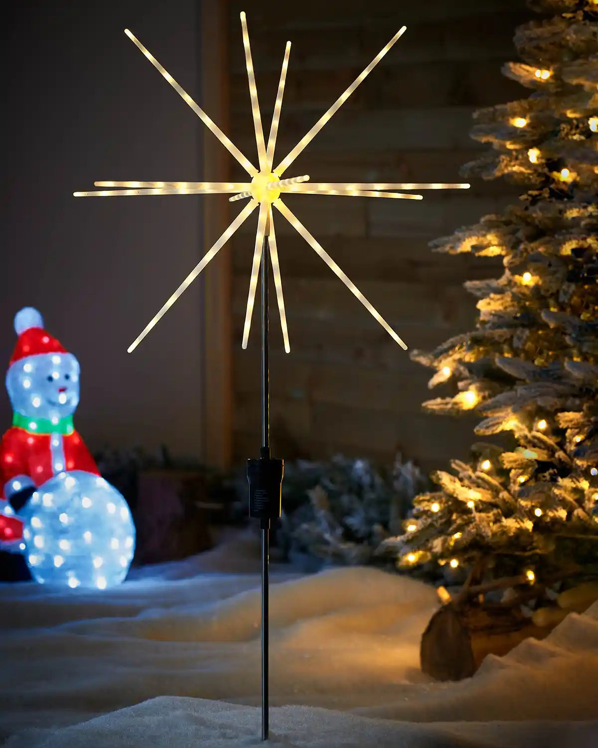 Starburst Pathway Stake Light, Warm White, 98 cm featuring 14 light tubes in a garden with Christmas tree and Snowman figurine 