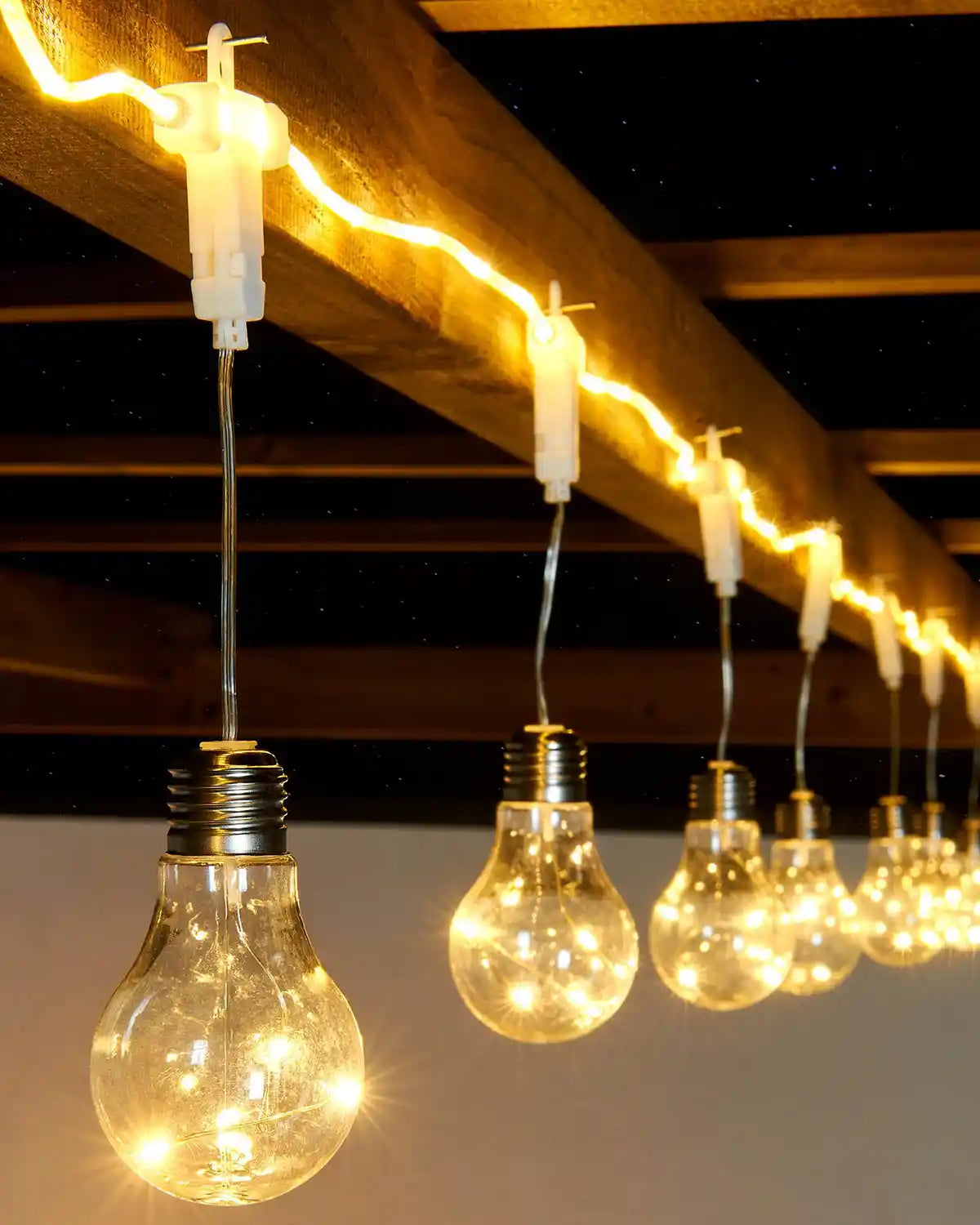 String of light bulbs hanging from a wooden beam with a dark ceiling background
