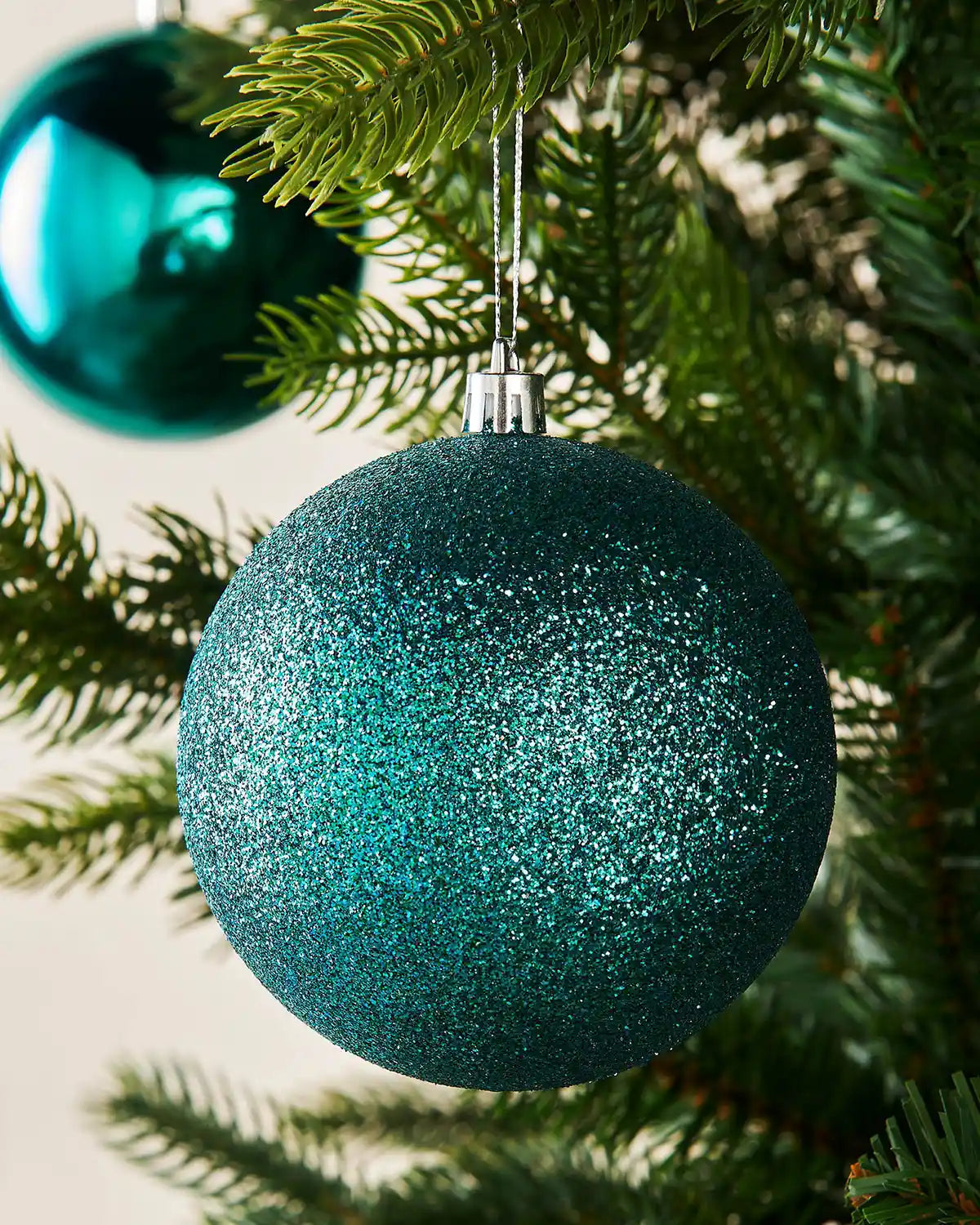 Teal glittery Christmas ornament hanging on a tree branch