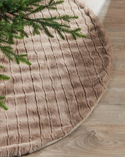 Textured beige Christmas tree skirt with green tree branches on a wooden floor.